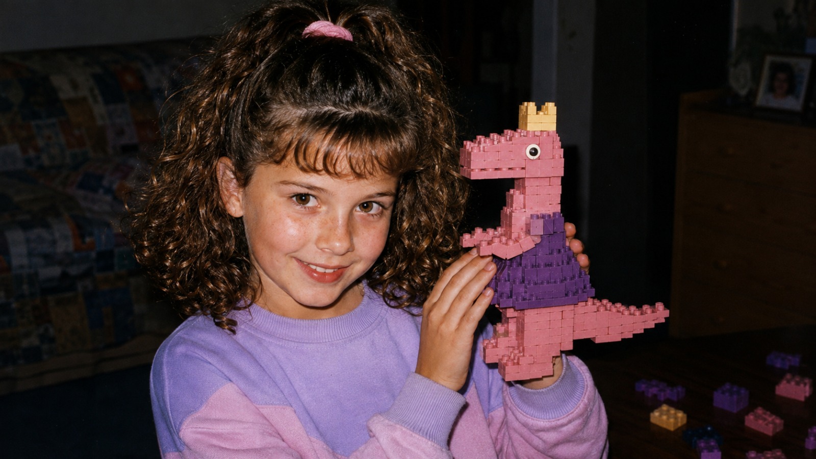 An 80s snapshot: a kid holding up the pink and purple dinosaur princess she built from toy bricks